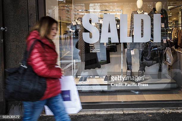 Woman walks past a shop window offering generous discounts during the winter sales in downtown Rome, Italy. The first day of winter sales in many...