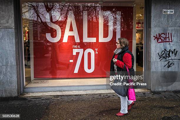 Woman walks past a shop window offering generous discounts during the winter sales in downtown Rome, Italy. The first day of winter sales in many...
