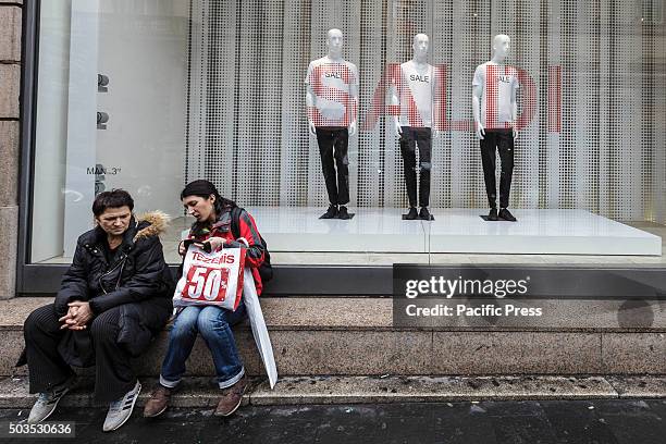 People sit near a shop window offering discounts during the winter sales in downtown Rome, Italy. The first day of winter sales in many Italian...