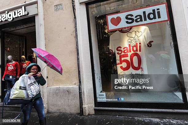 Woman walks past a shop window offering generous discounts during the winter sales in downtown Rome, Italy. The first day of winter sales in many...