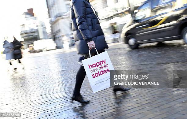 Woman walks holding a shopping bag reading "Happy Sales", on January 6, 2015 in Nantes, western France, on the first day of winter sales. / AFP /...