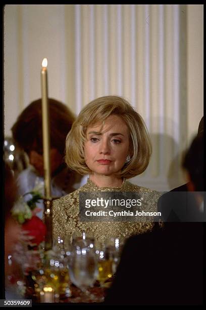 Somewhat downcast First Lady Hillary Rodham Clinton clad in lace, sitting in glow of taper during White House State Dinner honoring visiting Chilean...