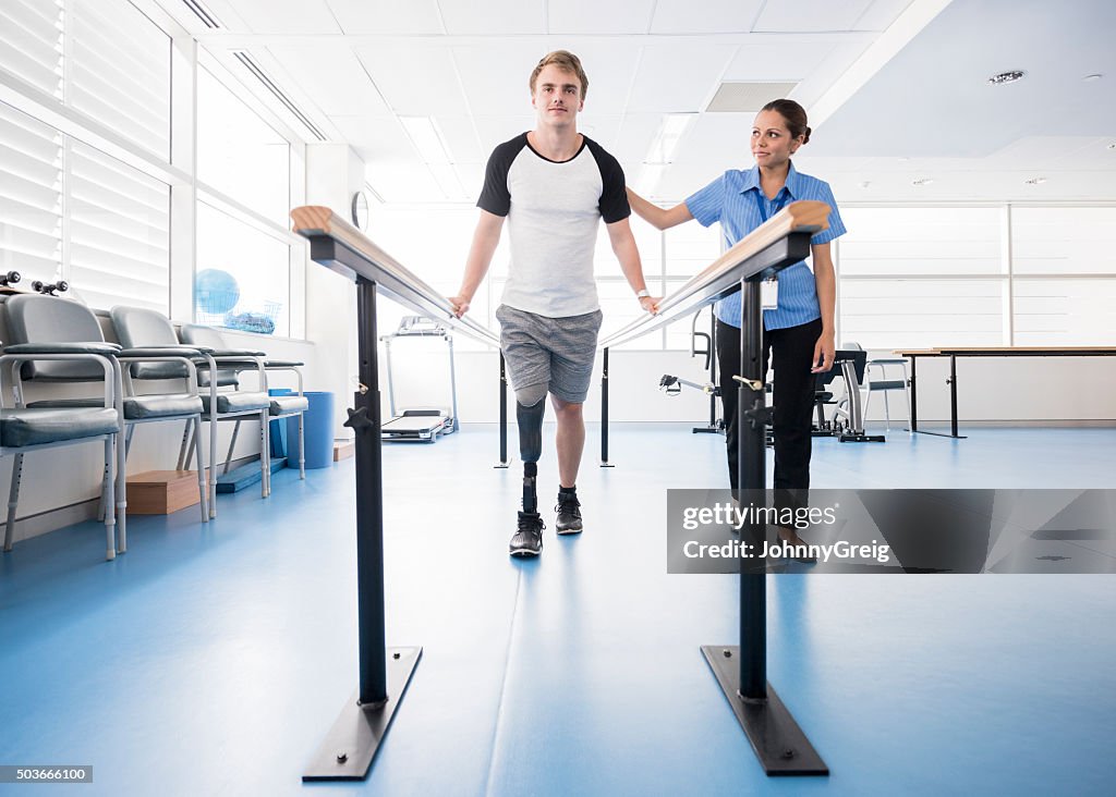 Man with prosthetic leg using parallel bars with physyiotherapist