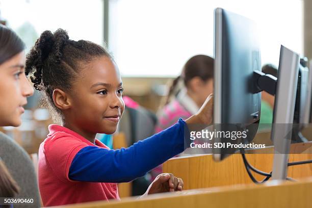 encantadores elemental edad las niñas el uso de ordenadores en las escuelas de la biblioteca - computer lab fotografías e imágenes de stock