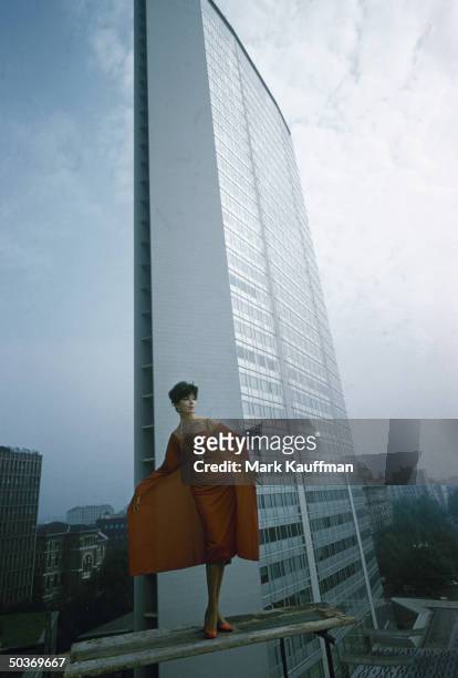 Model wearing red panelled cocktail dress by Italian designer Fabiani posing against backdrop of the Pirelli building, skyscraper designed by Gio...