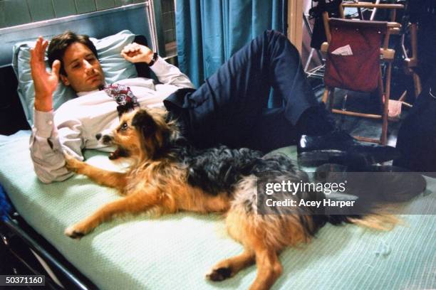 David Duchovny, co-star of cult hit TV series The X-Files, lying on bed w. Pet dog, in between filming, on the set of the show.