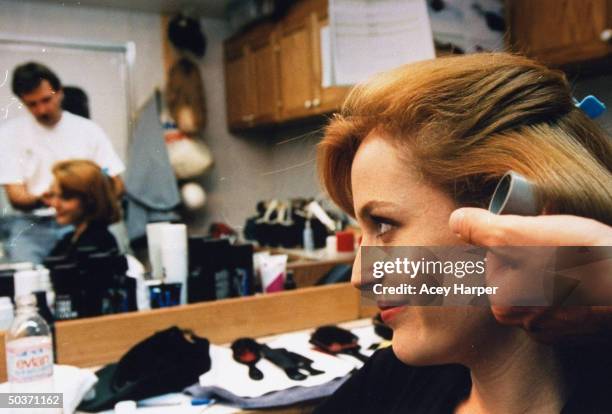 Gillian Anderson, co-star of cult hit TV series The X-Files, getting hair done by unident. Male stylist in dressing room on the set of the show.