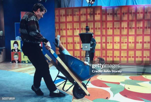 Talk show host Jim. J. Bullock wheeling co-host Tammy Faye Bakker Messner in wheelbarrow on the set of their show The Jim J. & Tammy Faye Show.