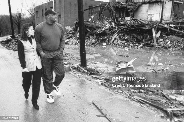 Pro football player Reggie White & wife Sara walking past burnt rubble of Inner City Church, where he acts as asst. Pastor.