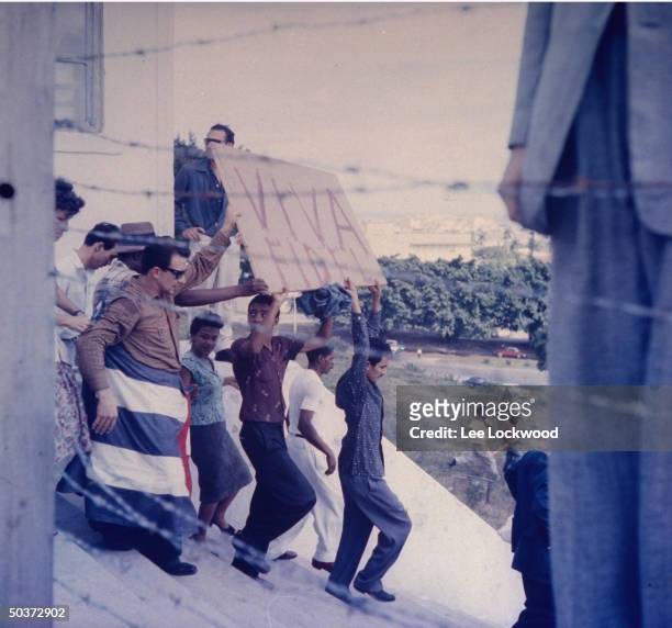 Jubilant population gathering in Havana w. Hand made sign reading: VIVA FIDEL and one person draped in Cuban flag as victorious Castro and rebel army...