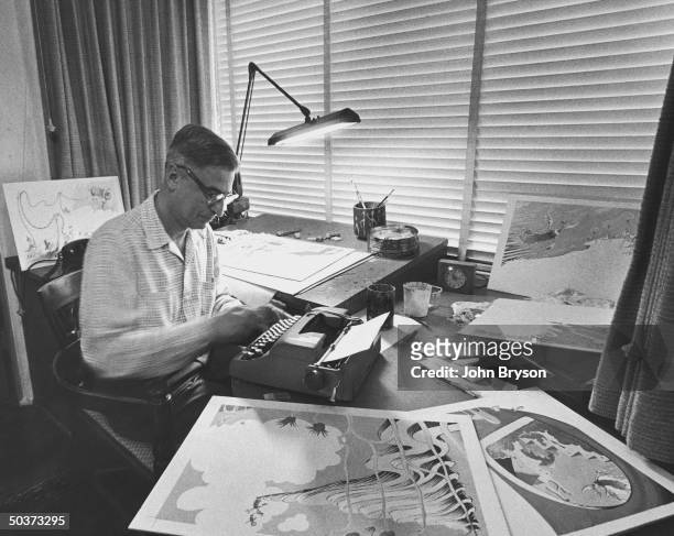 Children's book author Theodor Seuss Geisel working at his typewriter in his studio on a new book and surrounded by some of his illustrations for the...