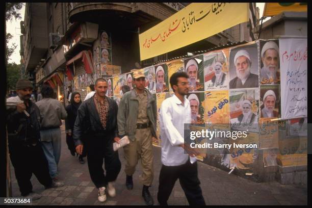 Pedestrians passing wall plastered w. Presidential election campaign posters picturing conservative cleric candidate Ali Akbar Nateq-Noori.