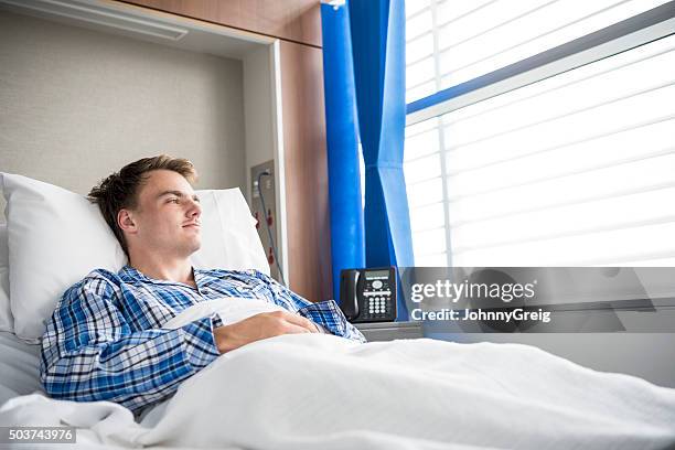 jeune homme reposant au lit d'hôpital regarder par la fenêtre - lit dhôpital photos et images de collection