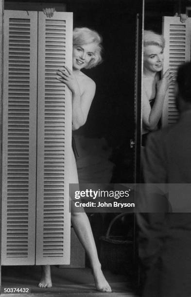 Actress Marilyn Monroe peering out at her husband Arthur Miller fr. Behind door after putting on sexy bikini bathing suit she purchased, w. The price...