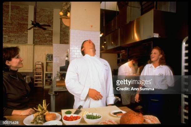 Chef Ben Ford, son of actor Harrison Ford, leaning back about to catch cherry tomato he threw in air with his mouth as co-workers watch at trendy...