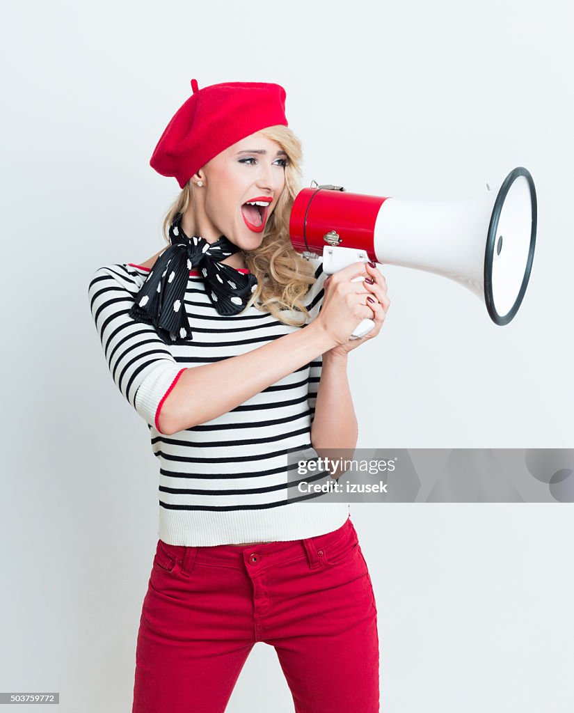 Happy french woman wearing red beret shouting into megaphone