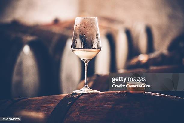 glass of white wine on a barrel in wine cellar - wijnglas stockfoto's en -beelden