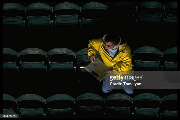 Aerial view of fan in stands sitting alone reading newspaper before game of Chicago White Sox vs Milwaukee Brewers.