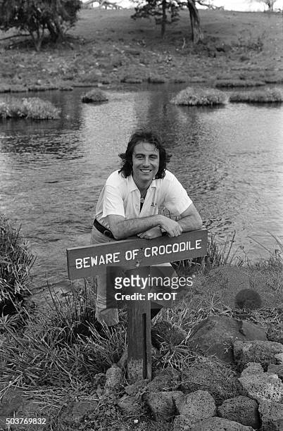 Le chanteur Michel Delpech en voyage au Kenya accoudé devant le panneau 'Beware of crocodile' en avril 1975.