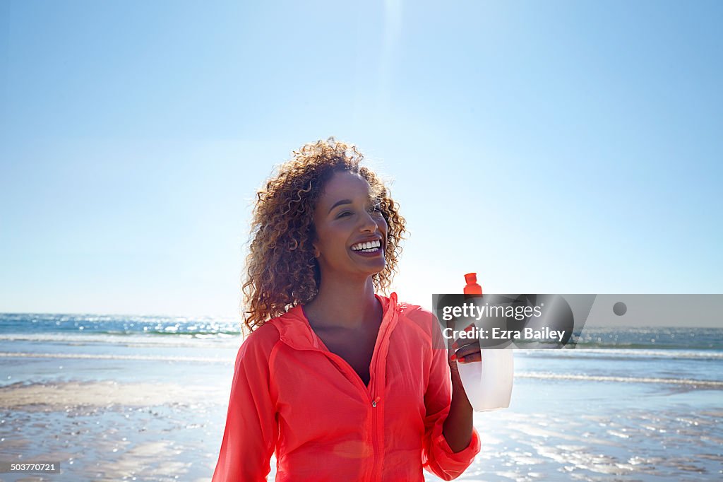 Woman exercising on the beach holding water bottle