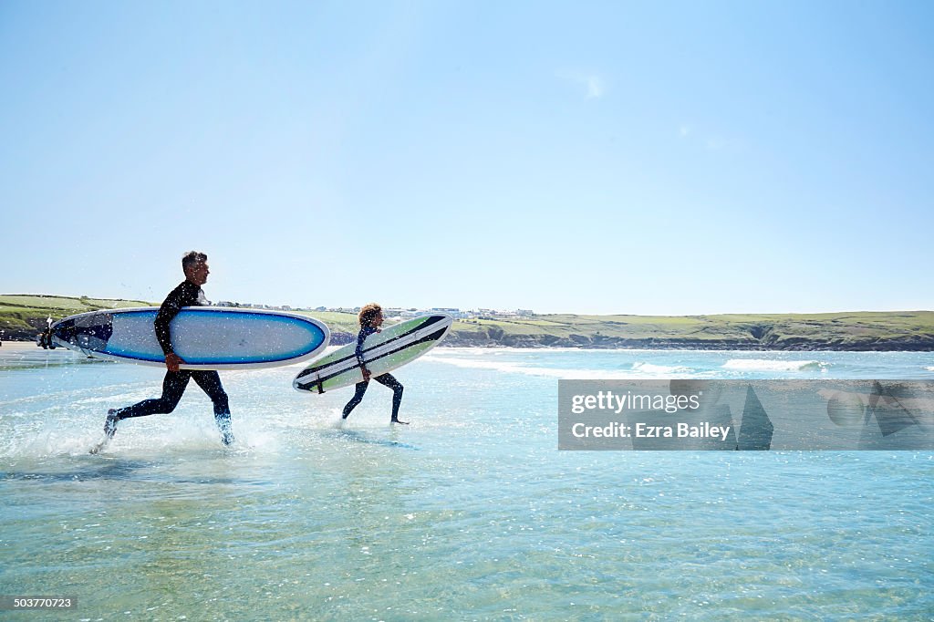 Surfers running into the waves with surfboards.