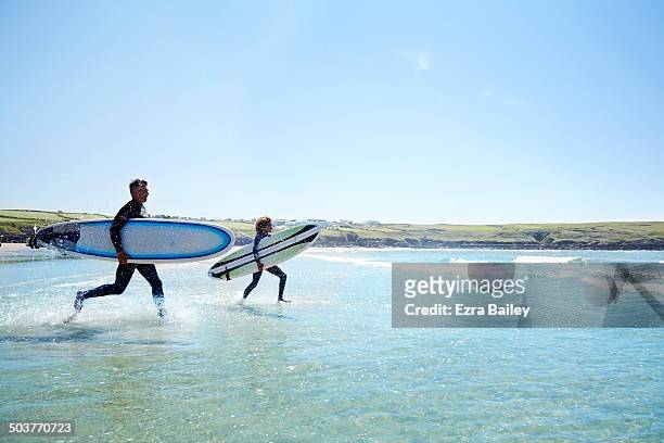surfers running into the waves with surfboards. - cornwall engeland stockfoto's en -beelden
