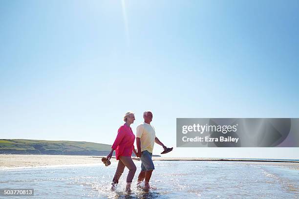 mature couple walking along a deserted beach. - ankle deep in water - fotografias e filmes do acervo