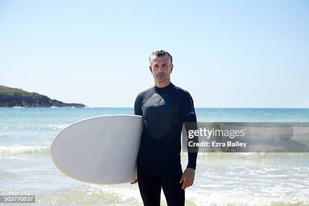 man in a wetsuit holding a surfboard. - man surfing photos et images de collection