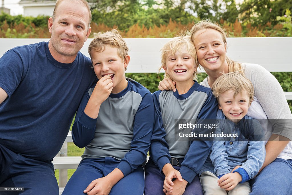 Familia de cinco posando sobre banco después de un partido de béisbol.