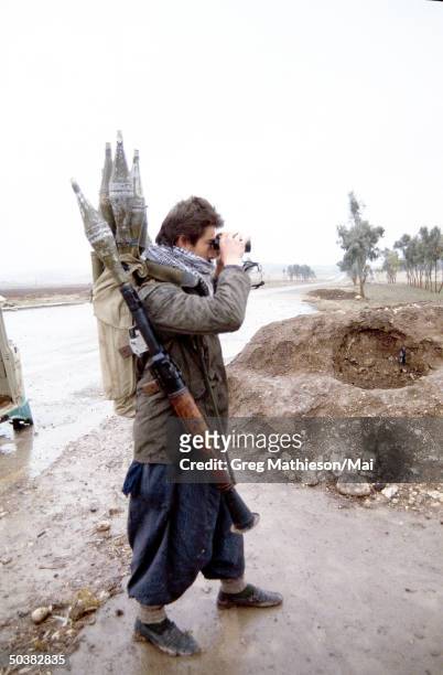 Kurdish Peshmerga soldier armed with the an RPG and rockets on his back, watching Iraqi military postions down the road. The Kurds are located within...