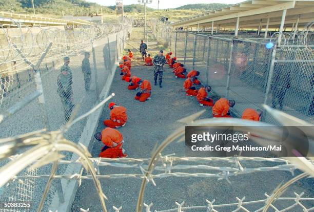 Taliban prisoners in orange jumpsuits sitingt in holding area under the watchful eyes of military police at Camp X-Ray at Naval Base Guantanamo Bay,...