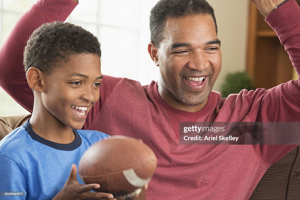 Black father and son watching sports in living room