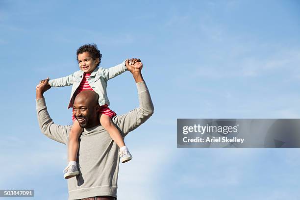 father carrying daughter on shoulders outdoors - mann mit kind auf den schultern stock-fotos und bilder