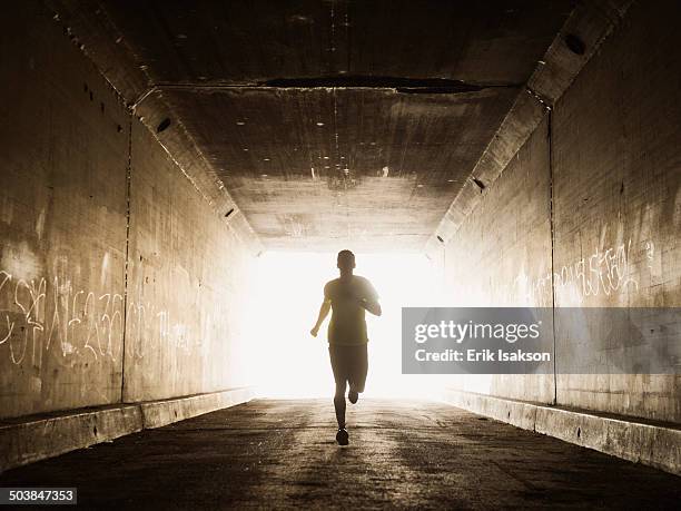 caucasian man running in urban tunnel - uithoudingsvermogen stockfoto's en -beelden