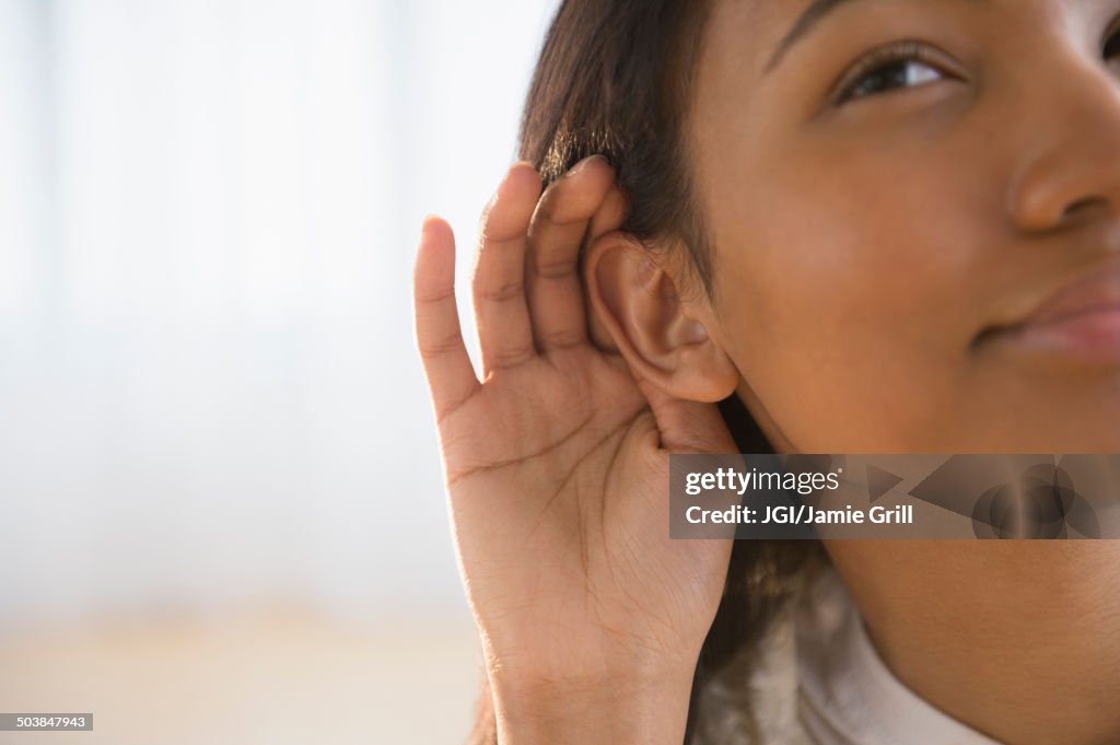 Mixed race woman cupping her ear