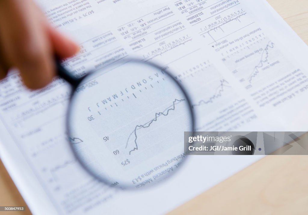 Mixed race woman reading graph with magnifying glass