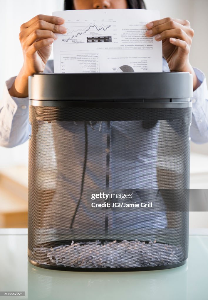 Mixed race businesswoman shredding documents