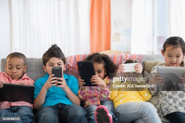 children using technology on sofa - boys mobile phone group stock pictures, royalty-free photos & images