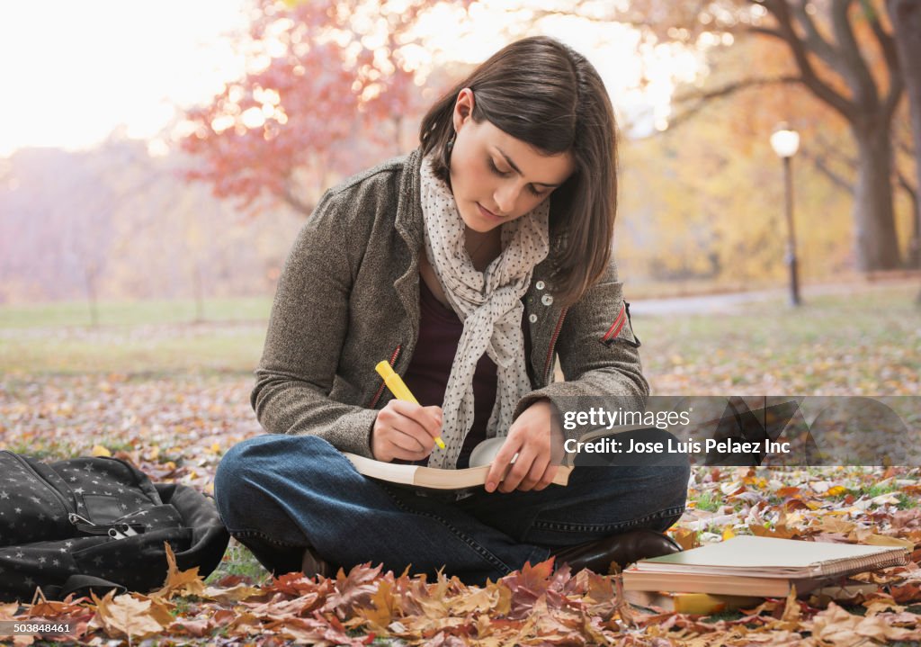 Caucasian student reading in park with autumn leaves