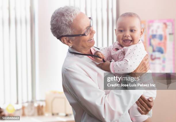 doctor holding baby in office - doctor and baby stock-fotos und bilder