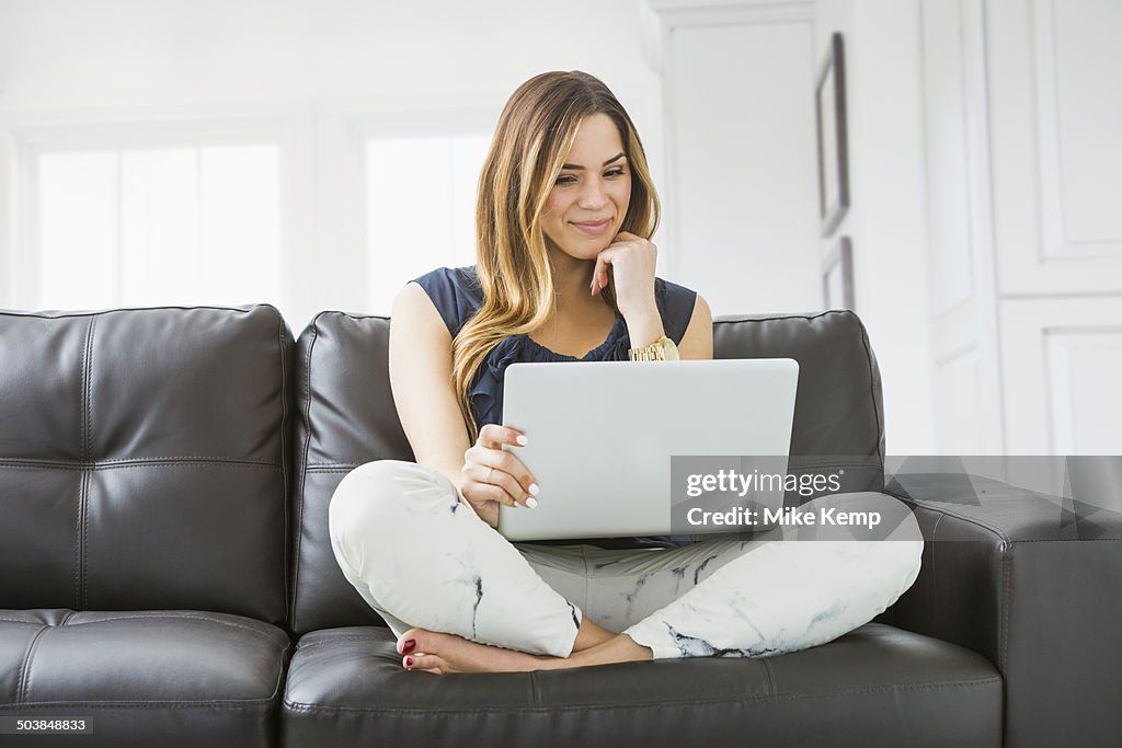 Mixed race woman using laptop on sofa