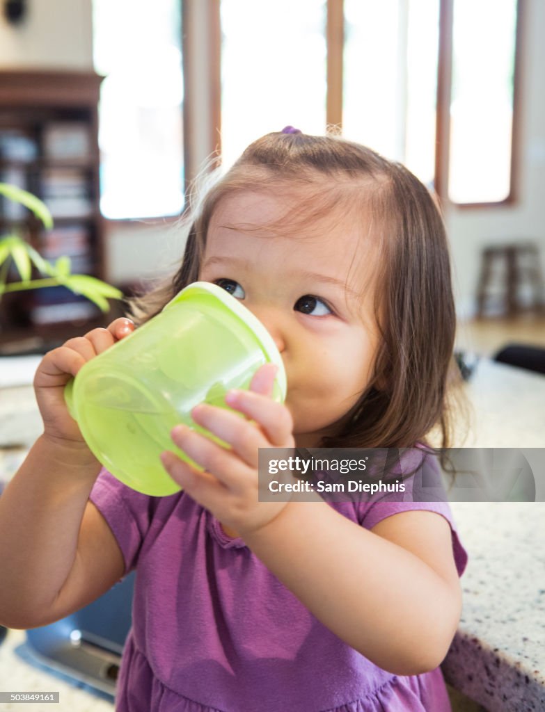 Mixed race girl drinking from sippy cup in kitchen