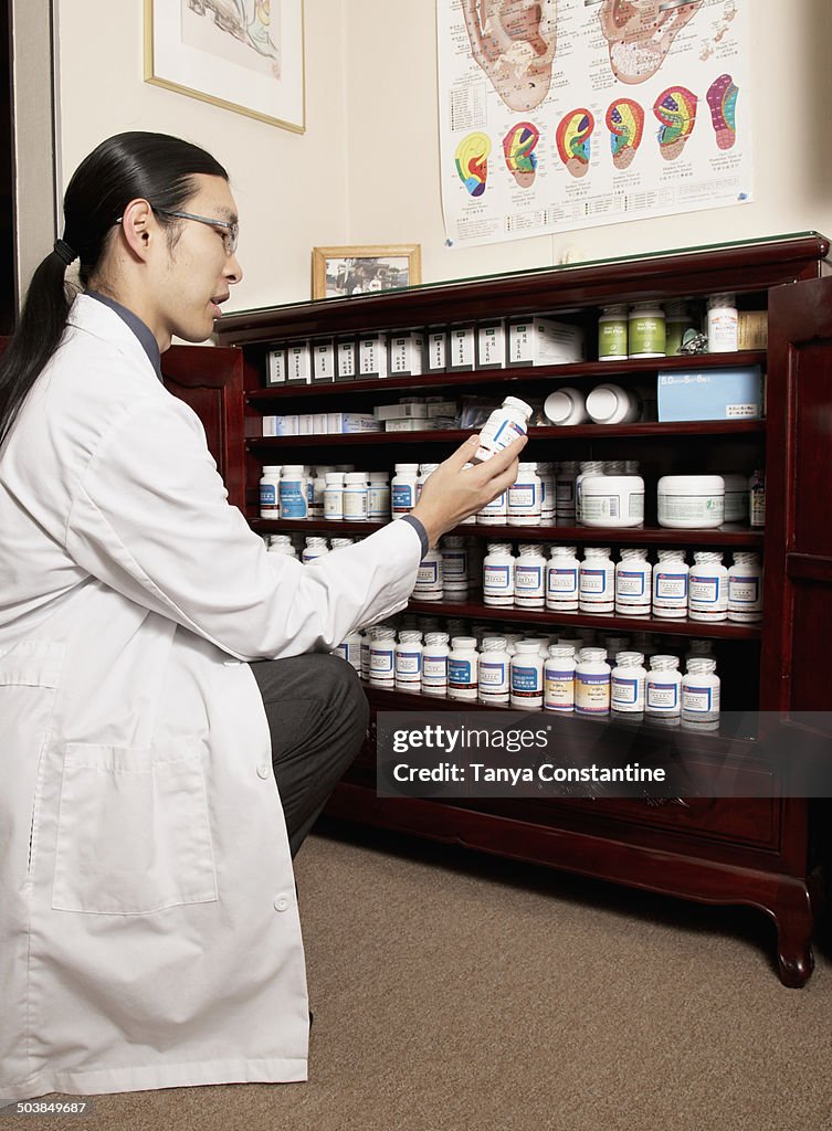 Chinese medicine practitioner selecting herbs from cabinet