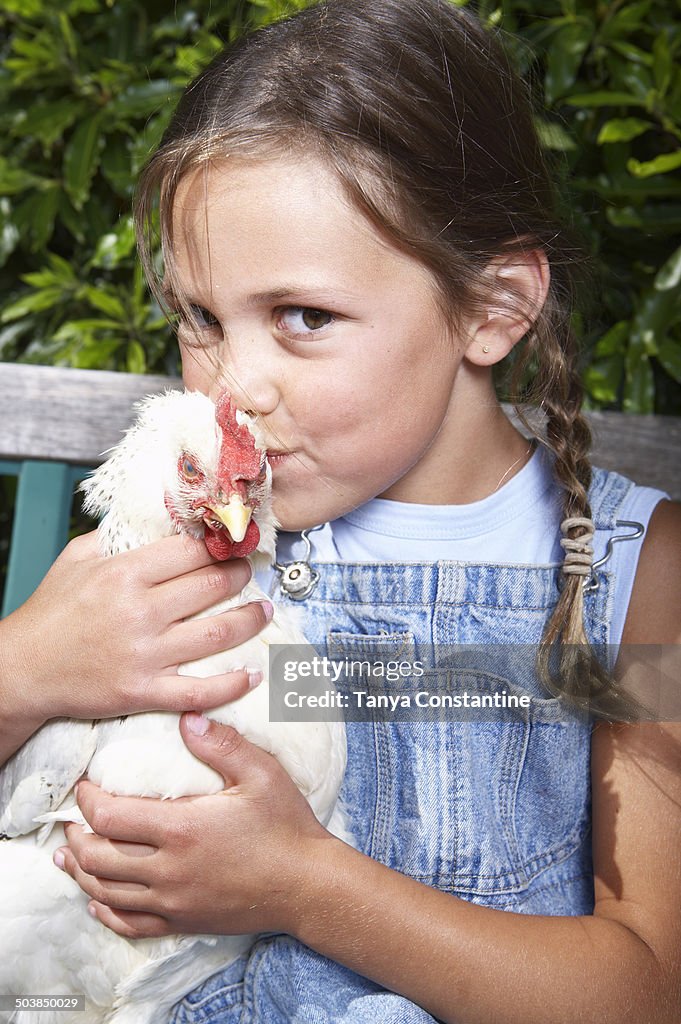 Mixed race girl kissing chicken on farm