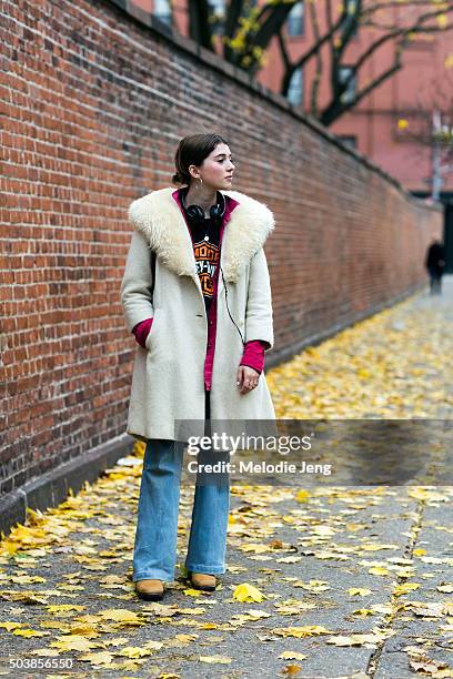 Elise Hoggard wears a vintage off-white coat with a fur collar, a cerise button-up shirt, Harley-Davidson t-shirt, light flared jeans, brown suede...