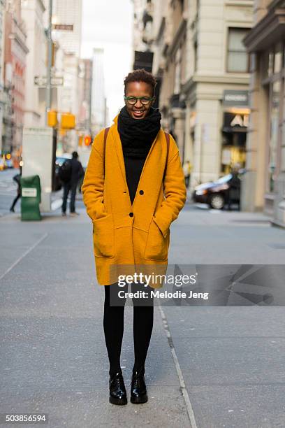 Student Thati Peele wears mustard cardigan jacket, green-framed glasses, a large black scarf, and black shoes mostly from Urban Outfitters on...