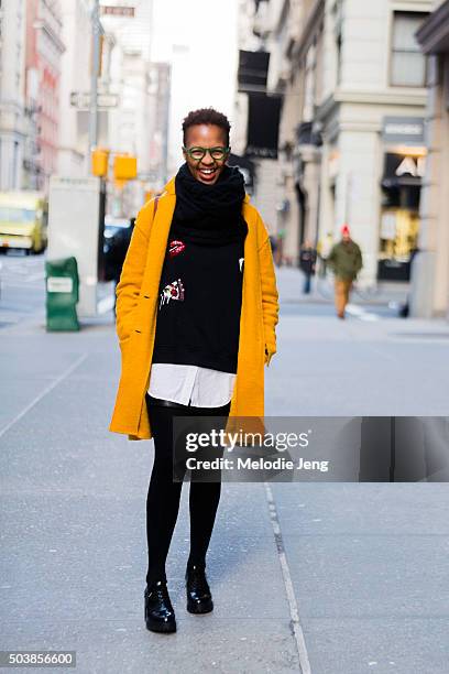 Student Thati Peele wears mustard cardigan jacket, green-framed glasses, a large black scarf, a black pizza-sequined sweater over a white button-down...