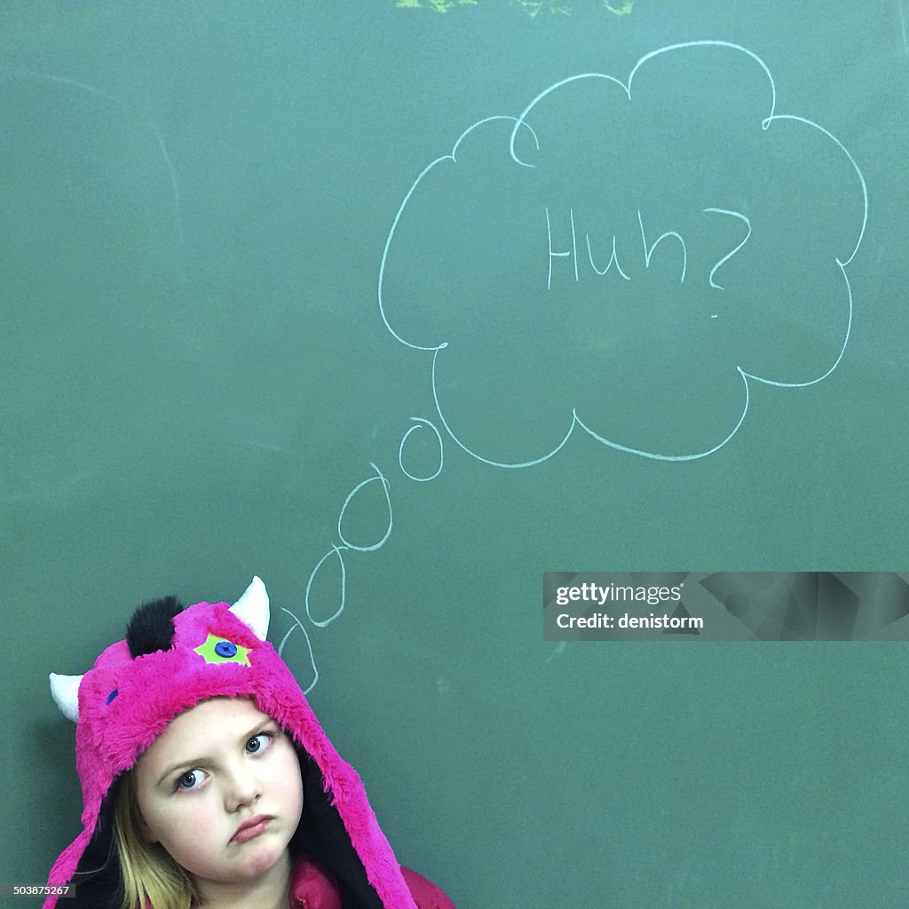 Portrait of a Girl standing in front of blackboard with puzzled expression