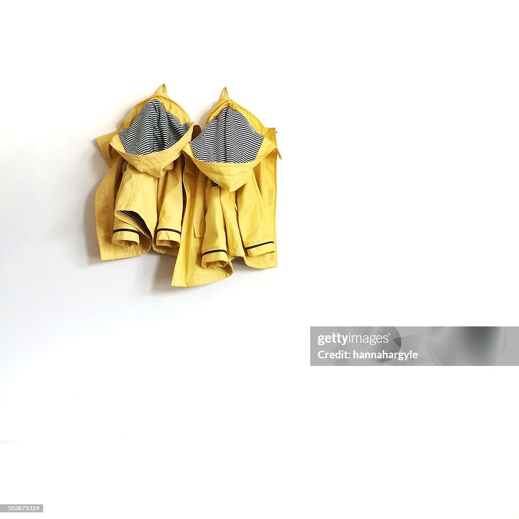 Two yellow raincoats hanging on wall