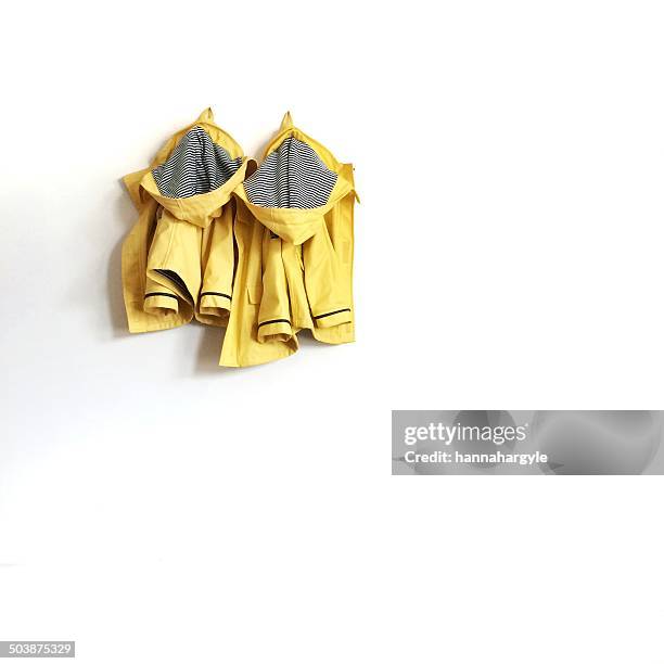 two yellow raincoats hanging on wall - coat hanging stock pictures, royalty-free photos & images